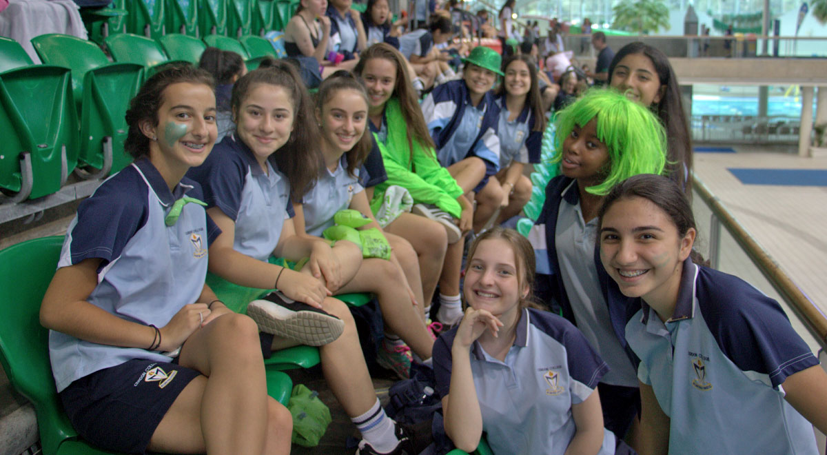 Group of smiling Cerdon College Merrylands students in the grandstand at the 2018 Swimming Carnival hosted Sydney Olympic Park Aquatic Centre.